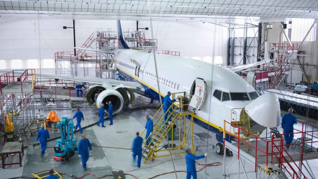 Avião em hangar de manutenção com mecânicos trabalhando.