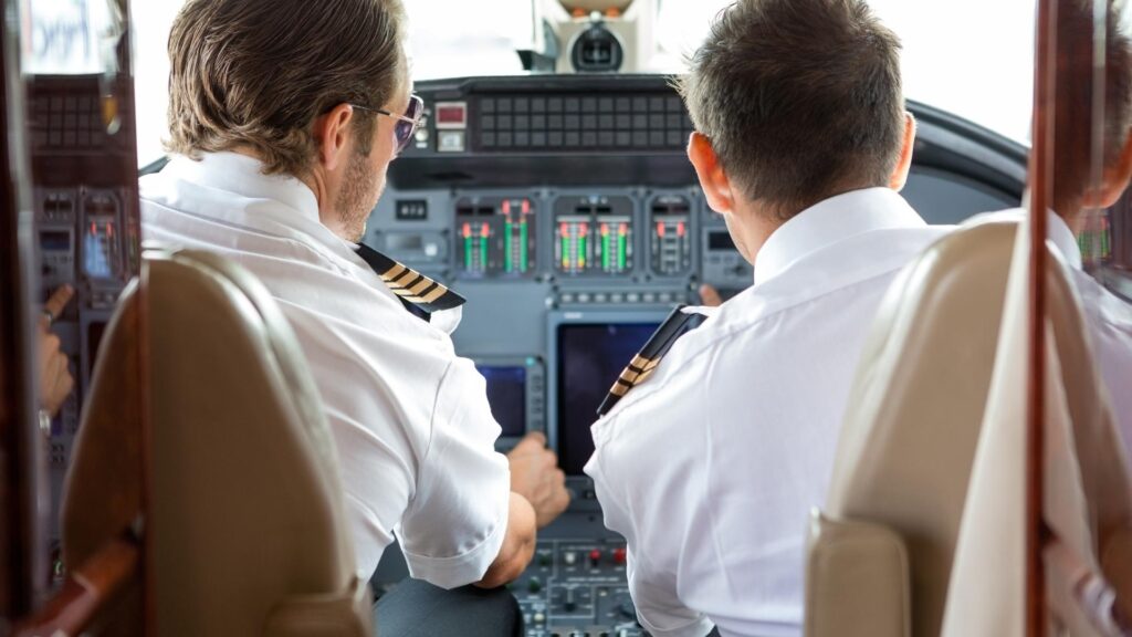 Pilotos conversando dentro da cabine de pilotagem de um jato executivo.