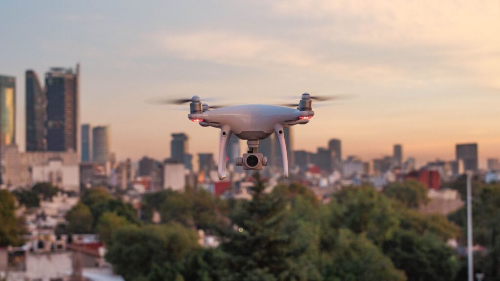 Drone de filmagem voando em meio ao horizonte de uma cidade no fim de tarde.