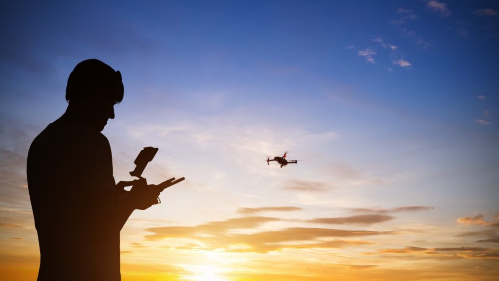 Slhueta de uma pessoa pilotando um drone que pode ser visto ao longe.