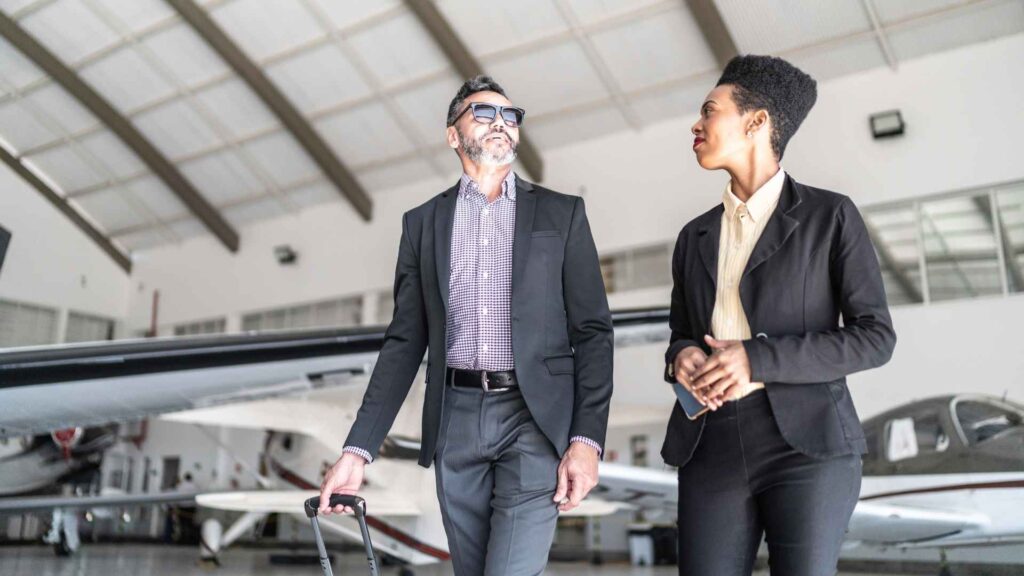 Uma mulher e homem caminhando em hangar com aviões de fundo